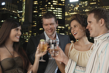 Two young couples toasting drinks against city skyline at night