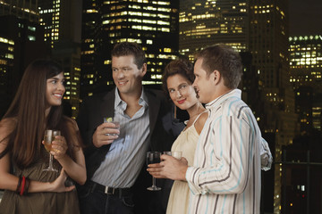 Two young couples drinking together against city skyline at night