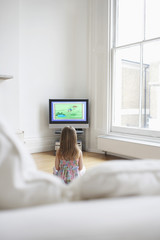 Obraz premium Rear view of a little young girl watching cartoons in television at home