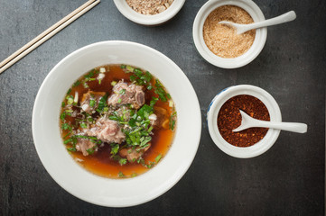 Asian style pork bone soup with seasoning on dark stone background