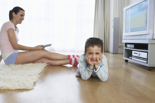 Young woman sitting on floor and watching television by her son