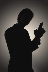 Side view of a silhouetted man making gun shaped gesture against gray background