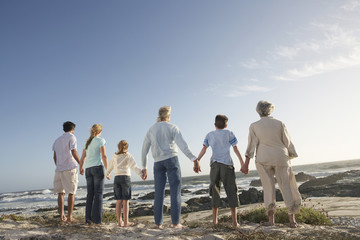 Rear view of three generation family holding hands on seashore - obrazy, fototapety, plakaty