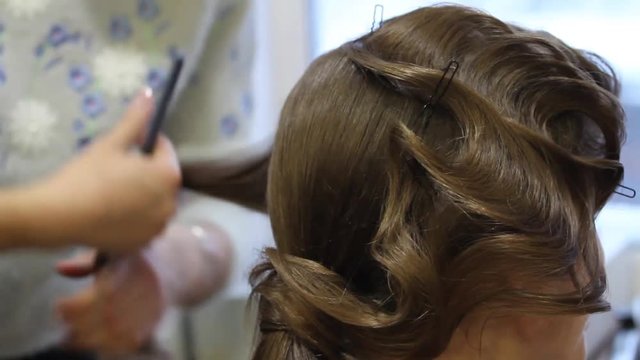 Hairdresser creating complicated evening and wedding hairstyles at barbershop salon. Close-up of hands corrects hair curls and strands