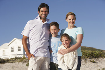 Portrait of happy family of four with beach house in background
