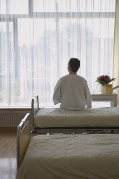 Rear View Of A Male Patient Sitting In Hospital Bed