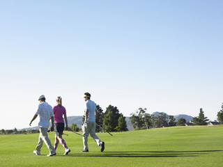 Rear view of three young golfers walking on golf course