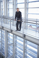 Full length portrait of happy middle aged businessman standing by railing in modern office