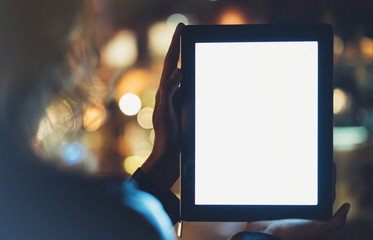 Girl holding in hands on blank screen tablet on background illumination glow bokeh light in night atmospheric christmas city, hands using template computer on lights glitter street; mockup gadget