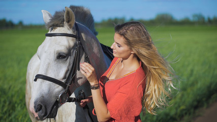 Obraz premium Beautiful blonde girl standing with a horse at a countryside