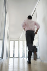 Rear view of young businessman running in corridor