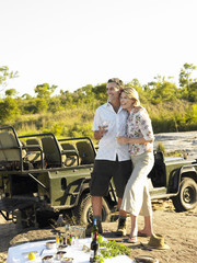 Smiling couple on picnic during safari with jeep in the background © MDBPIXS