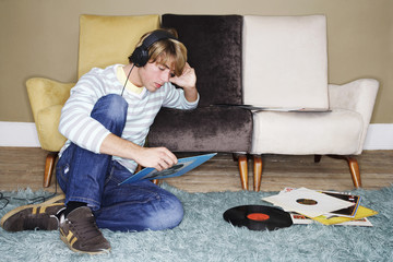 Young man sitting on rug and listening to records in the living room