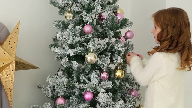Portrait of cute happy little girl helping her family to decorate Christmas tree in living room. Child hanging holiday decorations. Real time full hd video footage.