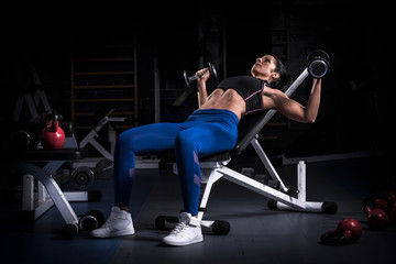 Fototapeta na wymiar Woman bodybuilder in gym lifting dumbbells on bench