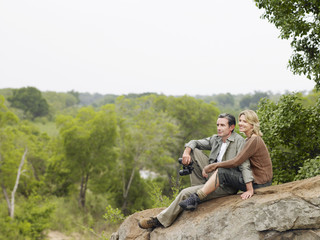 Smiling adult couple sitting on rock and enjoying the view