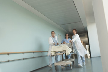 Low angle view of physicians rushing patient on gurney down hospital corridor