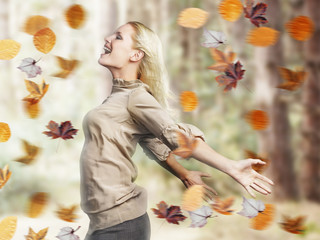 Side view of a happy young blond woman standing with arms outstretched amid autumn leaves