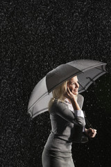 Side view of a smiling businesswoman using mobile phone under umbrella in rain