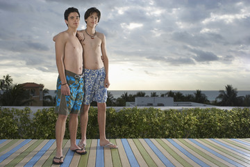 Full length portrait of two teenage friends standing on deck overlooking ocean