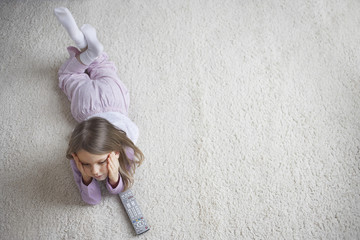 Top view of a little girl lying on rug with remote control