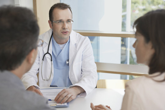 Smart doctor conversing with a cropped couple at hospital desk