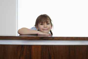 Naklejka premium Portrait of happy little girl resting head on wooden surface at home