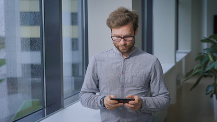 Bearded worker of the institute plays in the lobby on your smartphone.