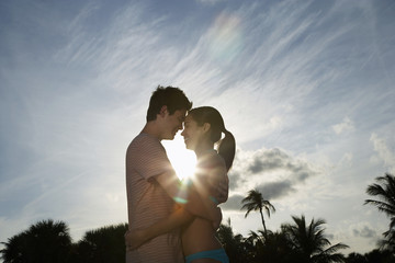 Side view of romantic teenage couple hugging on beach at sunset