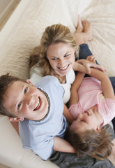 High angle view of cheerful young boy having fun with mother and sister on sofa