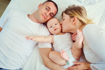 Fototapeta na wymiar Happy family. Mother, father and son, the child lying on bed. Top view of parents and baby boy