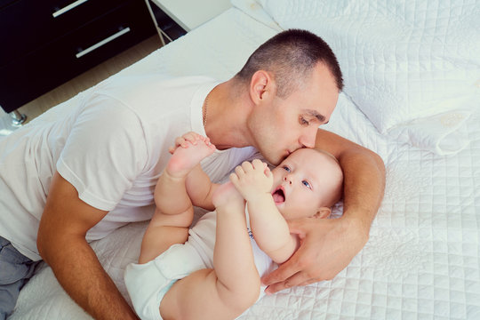 Dad with baby on the bed. Father kissing his little child cheek. Caring parents. Happy family.