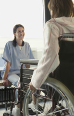 Young smiling female physician listening to patient in wheelchair