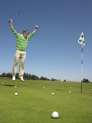 Full length of male golfer jumping with arms raised on putting green