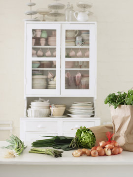 Closeup Of Fresh Vegetables And Paper Bag On Kitchen Counter With Utensils In Cupboard