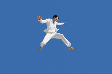 Fototapeta na wymiar Full length of young businessman jumping against blue sky