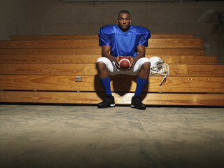 Portrait of an American football player sitting on bench with ball