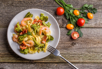 Pasta linguine with shrimps and broccoli in plate on wooden background.