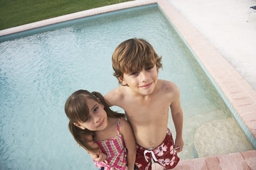 Portrait of little brother and sister standing arm around at the edge of swimming pool