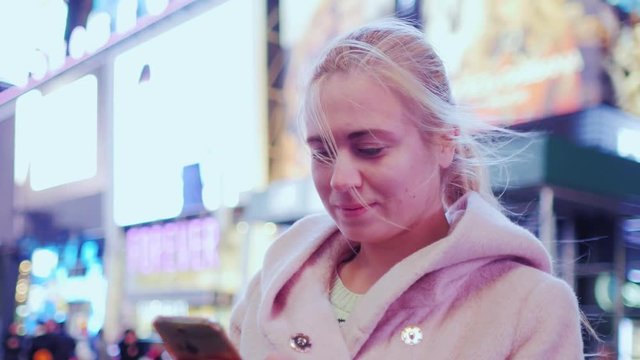 Young attractive woman in Times Square, New York, USA. Is typing text on the smartphone