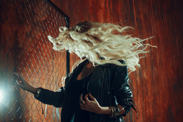 Naklejka premium Rock'n'roll girl, young beautiful woman dances in dark alley, against the fence mesh