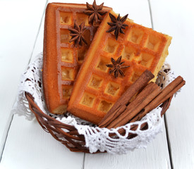 Freshly baked belgian waffles in wicker basket with christmas time spices on white wooden background. Perfect base for various desserts.