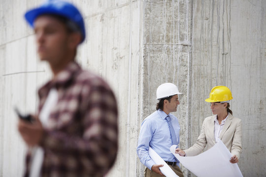 Managers with blueprint and blurred worker in foreground at construction site