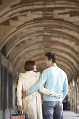 Rear view of a couple with arms round each other walking through archway 