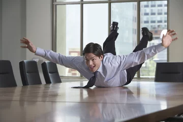 Foto op Canvas Young businessman sliding on stomach on conference table © moodboard