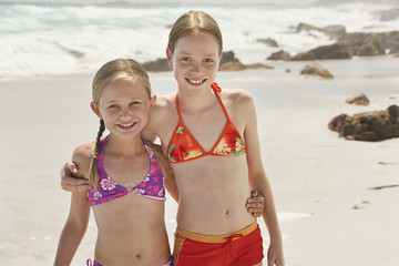 Portrait of happy little sisters standing with arms around on beach