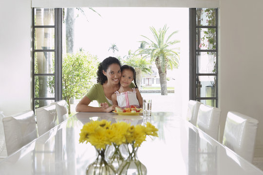 Portrait of smiling mother and daughter sitting at dining table