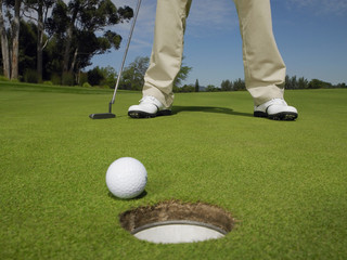 Low section of male golfer on green with ball at hole in foreground - Powered by Adobe