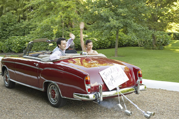 Happy bride and groom waving in retro convertible