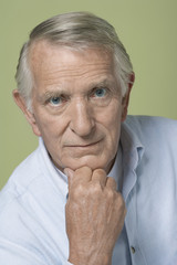 Portrait of a serious senior man with hand on chin over colored background